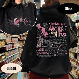 May include: Black hooded sweatshirt with a pink and white graphic on the back featuring a fox, bow and arrow, and text that reads "The Ballad of the Archer and the Fox." The Gildan brand logo is visible.
