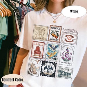K&ouml;nnte beinhalten: Wei&szlig;es Comfort Color T-Shirt mit Fantasy-Postwertzeichen-Designs. Die Briefmarken zeigen einen Greif, einen Thron, einen Drachen und andere Fantasy-Elemente. Der Text enth&auml;lt "POROMIEL", "ARETIA", "QUEST SQUAD" und "FLY OR DIE".
