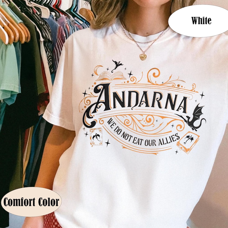 May include: White t-shirt with the word "ANDARNA" in a decorative font, accompanied by illustrations of a book, bats, and cards. The text "WE DO NOT EAT OUR ALLIES" is below the main text. The shirt is labeled "Comfort Color".