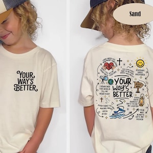 May include: Sand-colored t-shirt with the text "YOUR WAY'S BETTER" on the front and a graphic design on the back. The back design includes text and illustrations, such as a heart, a cross, and a smiley face.