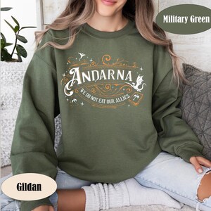 May include: Military green sweatshirt with the word "Andarna" in a decorative font, along with the phrase "We do not eat our allies." The Gildan brand is visible. The design includes a dragon and other decorative elements.