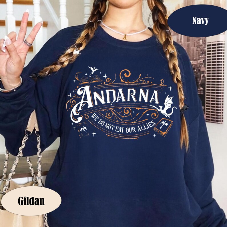 May include: Navy blue sweatshirt with the word "Andarna" in a decorative font, along with the phrase "We do not eat our allies." The design includes ornate swirls, stars, and small illustrations. The sweatshirt is a Gildan brand.