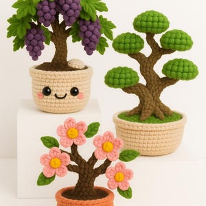 Peut inclure: Trois bonsaïs crochetés en pot. L'un a des raisins violets, un autre des feuilles vertes et le troisième des fleurs roses. Les pots ont des visages souriants. Les arbres sont sur une surface blanche.