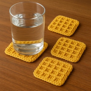 May include: A clear glass of water sits on a square, yellow crocheted coaster. Three additional yellow coasters are arranged on a wooden surface. The coasters have a textured, waffle-like pattern.