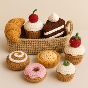 May include: A collection of crocheted baked goods, including a croissant, cupcakes with cherries and strawberries, a slice of cake, a cinnamon roll, a pie, and a donut. The items are in a woven basket and on a light background.