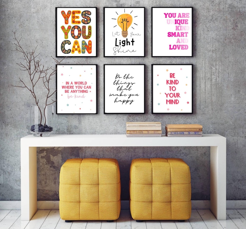 May include: A collection of framed art prints with inspirational quotes. The prints feature colorful text on white backgrounds, including phrases like "Yes You Can" and "Let Your Light Shine." The arrangement includes a white console table and two yellow square ottomans.