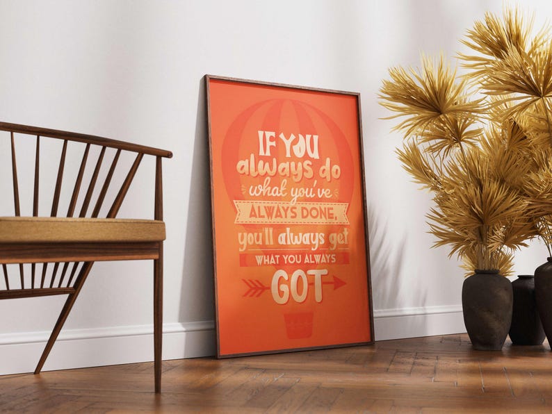 May include: An orange framed poster with the text "IF YOU always do what you've ALWAYS DONE, you'll always get WHAT YOU ALWAYS GOT". A wooden chair and decorative dried plants in black vases are also visible.