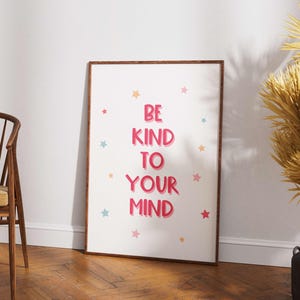 May include: A framed poster with the words "BE KIND TO YOUR MIND" in pink, surrounded by colorful star illustrations. The poster has a wooden frame and is displayed against a white wall.
