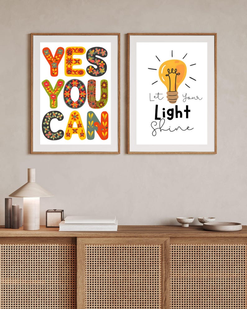 May include: Two framed art prints. One print says "YES YOU CAN" in colorful, floral-patterned letters. The other print features a yellow lightbulb with the words "Let Your Light Shine". Both prints are in wooden frames.