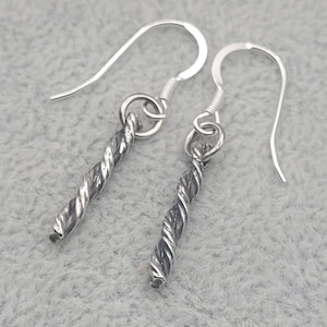 May include: A pair of silver-colored earrings. Each earring features a twisted, textured design suspended from a simple hook. The earrings are displayed against a light gray background.