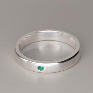 Op de afbeelding: Een zilveren ring met een kleine, ovale smaragd. De ring heeft een gepolijst oppervlak en een minimalistisch ontwerp. De smaragd is in het midden van de ring gezet. Een klassiek sieraad.