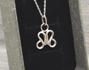 May include: A silver-colored pendant necklace with a unique, abstract design. The pendant is in the shape of a stylized butterfly or bow, suspended from a delicate chain. The necklace is presented in a gray gift box with a black interior.
