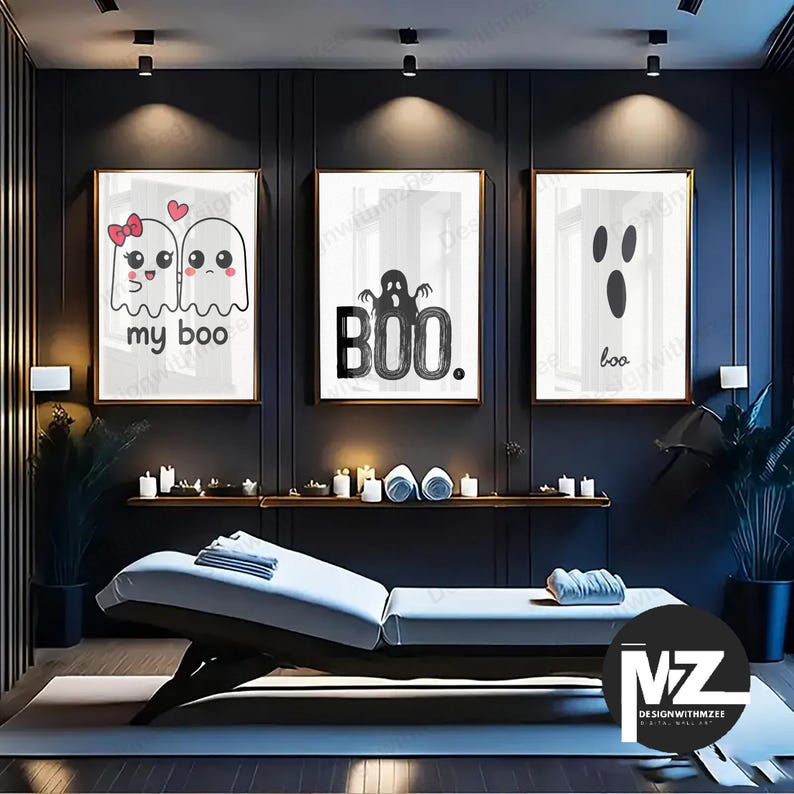 May include: Three framed Halloween-themed art prints. The prints feature ghost illustrations with the phrases "my boo" and "boo." The artwork is in black and white with gold frames. The room has a dark color scheme with a massage table and candles.