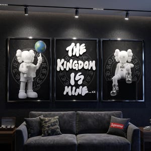 May include: A triptych of framed wall art featuring white cartoon figures with X-shaped eyes on a black background. The left panel shows a figure balancing a globe on one finger. The center panel displays the white text THE KINGDOM IS MINE...xx.