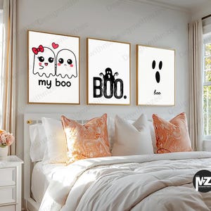 May include: Three framed art prints with gold frames hang above a bed. The prints feature white backgrounds with black graphics and text. One says "my boo" with ghost illustrations, another says "BOO", and the last says "boo".
