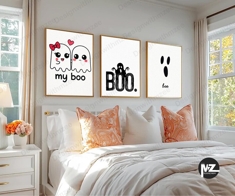 May include: Three framed art prints with gold frames hang above a bed. The prints feature white backgrounds with black graphics and text. One says "my boo" with ghost illustrations, another says "BOO", and the last says "boo".
