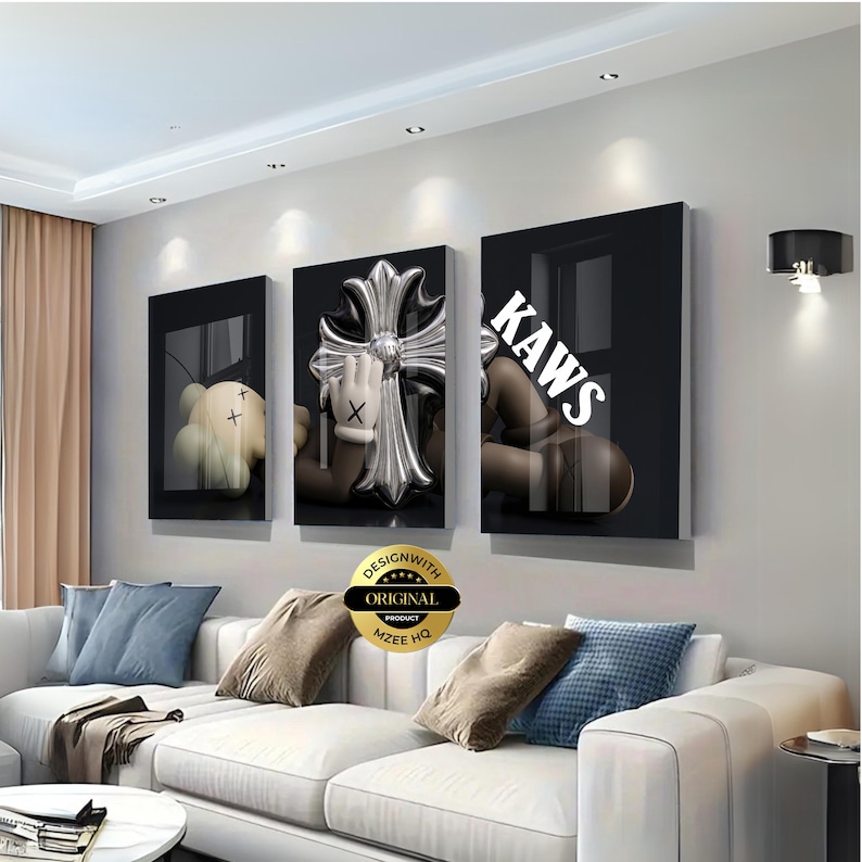 May include: A set of three rectangular wall art panels featuring a black background with a brown cartoon character with X-shaped eyes, a metallic silver cross emblem, and the white text KAWS printed across the right panel in a bold font.