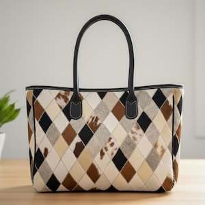 May include: A tote bag with a geometric pattern of diamonds in black, brown, cream, and tan. The bag has black leather handles and trim. The bag is sitting on a wooden surface.