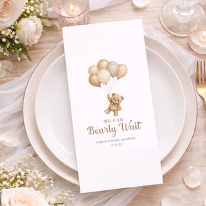 May include: A white rectangular card featuring a watercolor illustration of a brown teddy bear holding a cluster of beige and polka-dot balloons. The text reads WE CAN Bearly Wait, SARAH'S BABY SHOWER, and the date 12.06.26 in brown lettering.