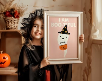 May include: A framed print with the text "I AM BOO-TIFUL" and a cartoon ghost wearing a witch hat and holding a jack-o'-lantern bucket. The print is held by a child dressed in a black costume with a lace headpiece, with an orange pumpkin in the background.