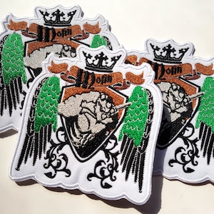 Puede incluir: Tres parches bordados blancos con un diseño negro y verde. Los parches presentan una corona, alas y el texto "12 oz" en una pancarta marrón.