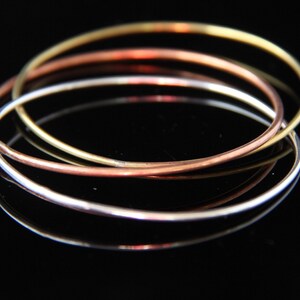 May include: Three interlocking metal bangles, one gold, one copper, and one silver.