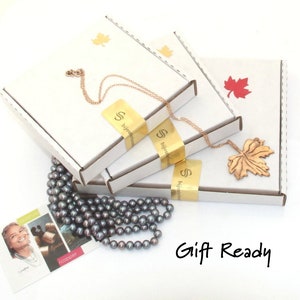 Puede incluir: Tres cajas de cart&oacute;n blanco con pegatinas de logotipo dorado y detalles de hojas de arce, un collar de cadena color cobre con un colgante de hoja de arce texturizado y un collar de perlas gris oscuro. Una tarjeta peque&ntilde;a con texto y Gift Ready.