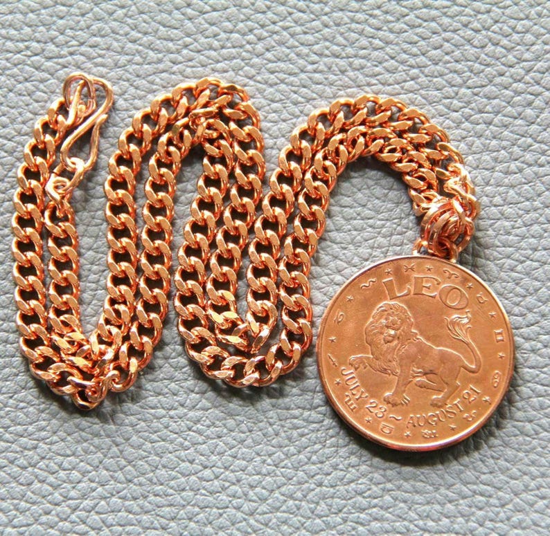 May include: A copper-colored necklace with a large round pendant. The pendant features a lion illustration and the word "LEO" at the top, with the dates "July 23 ~ August 21" below. The chain is a curb style.