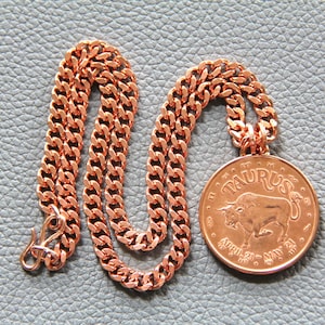 May include: A copper necklace with a copper pendant featuring the zodiac sign Taurus. The pendant has the text "Taurus" and "April 20 - May 20" inscribed on it.