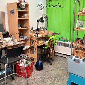 May include: A workshop interior with workbenches, shelves, and tools. A green backdrop is visible, along with a red crate and a blue tote bag. The words "My Studio" are written on the wall.