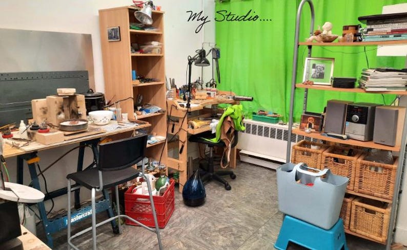 May include: A workshop interior with workbenches, shelves, and tools. A green backdrop is visible, along with a red crate and a blue tote bag. The words "My Studio" are written on the wall.