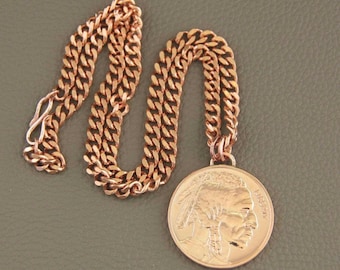 Puede incluir: Un collar de color oro rosa con una cadena de eslabones y un colgante redondo. El colgante muestra el perfil en relieve de una persona con un tocado, con la palabra LIBERTY grabada en el lado derecho de la pieza metálica circular.