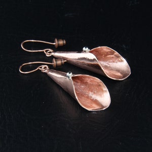 Puede incluir: Un par de pendientes de oro rosa con un diseño único, curvado, en forma de pétalo. Los pendientes tienen un estilo simple y minimalista.
