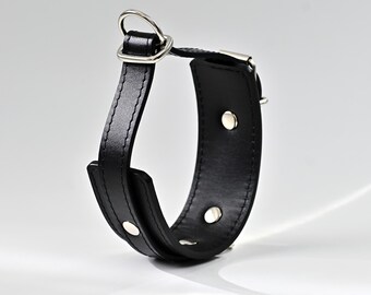 May include: A black leather wrist cuff with a silver-colored metal ring and rivets. The cuff is curved and has a stitched edge. The metal ring is attached to a rectangular piece of leather.