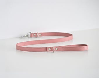 May include: A pink leather dog leash with a silver-colored clasp and hardware. The leash is a solid color and has a loop handle. The leash is made of a smooth material and is designed for pet owners.