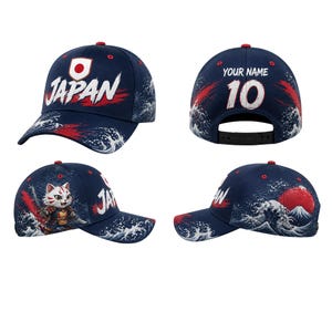 May include: Navy blue baseball cap with Japanese-themed designs. Features the word "JAPAN" in white, a red sun, and a wave pattern. The back has "YOUR NAME" and the number "10". A cat in samurai armor is on the side.