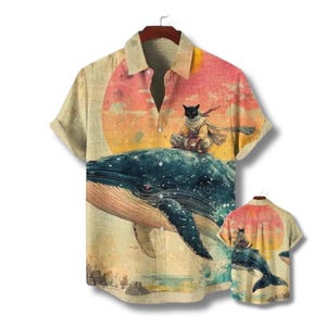 Può includere: Camicia a maniche corte con bottoni e un design stravagante. La camicia presenta un gatto nero che cavalca una balena su uno sfondo di tramonto. Il disegno è ripetuto su una camicia più piccola. La camicia è beige con colletto e bottoni.