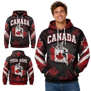 Op de afbeelding: Een zwarte hoodie met een rood-witte kaart van Canada met een esdoornblad, het woord CANADA in witte blokletters en rode esdoornbladpatronen. Het ontwerp bevat witte trekkoorden, een kangoeroezak aan de voorzijde en geribbelde boorden.