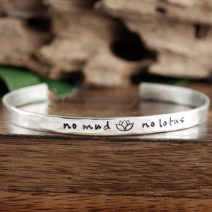May include: Silver bracelet with a hammered finish and the inscription "no mud no lotus" with a lotus flower symbol.