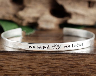 May include: Silver bracelet with a hammered finish and the inscription "no mud no lotus" with a lotus flower symbol.