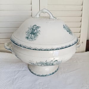 Peut inclure: Une soupière en céramique blanche avec couvercle assorti, ornée d'illustrations en transfert vert foncé représentant des enfants dans des décors extérieurs. Elle possède deux anses latérales, une base piédouche et une bordure décorative verte.