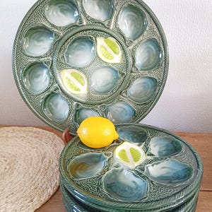 Könnte beinhalten: Grüne Keramik-Austernplatten mit muschelförmigen Fächern. Die Platten haben ein strukturiertes Design und einen seilartigen Rand. Eine ganze Zitrone und Zitronenscheiben sind auf den Tellern platziert.