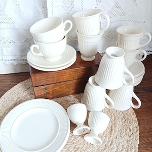 Peut inclure: Ensemble de vaisselle en céramique blanche comprenant tasses à thé, soucoupes, assiettes et coquetiers. Les tasses et les assiettes présentent un motif côtelé. Les articles sont disposés sur une boîte en bois et un tapis tissé.