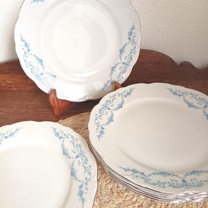 Peut inclure: Ensemble d'assiettes en porcelaine blanche avec un bord festonné et un motif floral bleu délicat. Les assiettes sont disposées sur une surface en bois, mettant en valeur leur esthétique élégante. Idéal pour servir les repas.