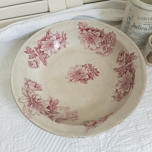 Könnte beinhalten: Eine runde Keramikschale in cremeweißer Grundfarbe mit einem dunkelroten floralen Transferdruckmuster. Das Design zeigt Gruppen detaillierter Blumen und Blätter am inneren Rand sowie ein einzelnes florales Motiv in der Mitte.
