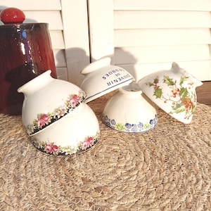 Puede incluir: Una colección de cuencos de cerámica vintage con diseños florales y botánicos. Un cuenco está apilado sobre otro. Algunos cuencos tienen el texto "SOUVENIR DE LOURDES". Los cuencos están dispuestos sobre una estera tejida.