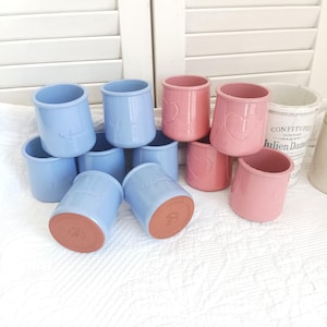 May include: A collection of small ceramic pots in light blue and pink. The blue pots feature the embossed text "la fermière" and the pink pots feature an embossed heart design. Each pot has a terracotta-coloured base and a smooth, glazed finish.