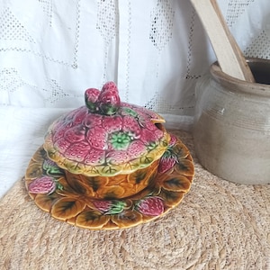 Puede incluir: Un plato para servir de cerámica con forma de fresa con tapa y plato a juego. El plato es principalmente rosa con detalles en verde y amarillo, y presenta un diseño detallado de fresa. El plato y la tapa están adornados con motivos de fresas y hojas.