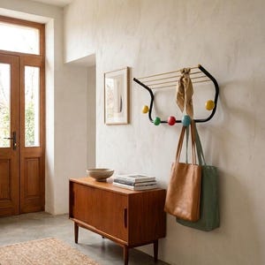 Könnte beinhalten: Ein Eingangsbereich im Mid-Century-Modern-Stil mit einem Holzschrank, einem gewebten Teppich und einer Wandgarderobe. Die Garderobe hat einen schwarzen Rahmen mit bunten Knöpfen und hält einen Schal und zwei Tragetaschen. Ein gerahmtes Kunstwerk hängt an der Wand.