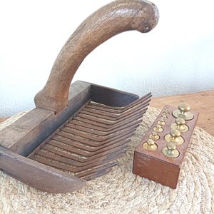 Puede incluir: Antigua paleta de mantequilla de madera con un mango curvo y una serie de cuchillas paralelas. Una pequeña caja de madera contiene pesas de latón de varios tamaños. Los artículos se exhiben sobre una estera tejida.